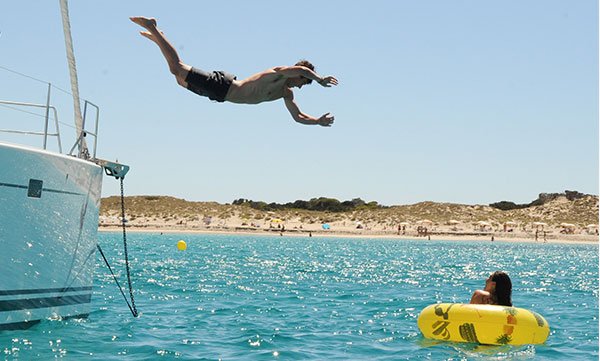A person joyfully jumping off a Formentera charter yacht into the blue sea