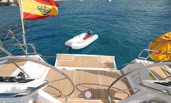Stern view of a Formentera charter yacht with the Spanish flag flying and a dinghy attached