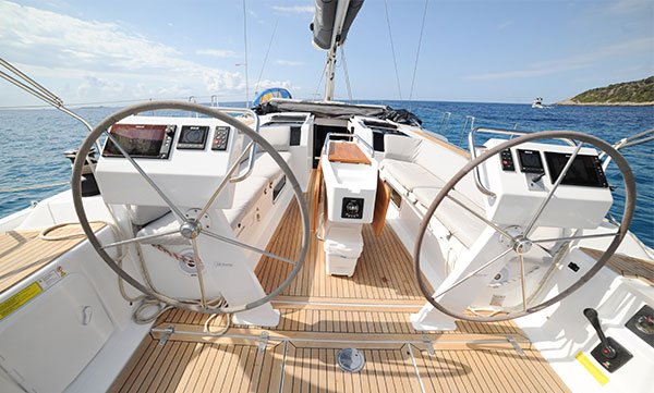 Dual steering wheels at the command bridge of a Formentera charter yacht with the open sea and coastal view
